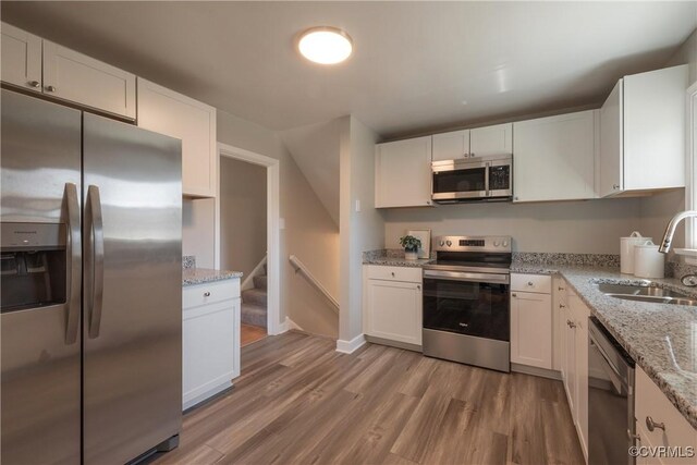 kitchen with white cabinets, light stone counters, a sink, light wood-style floors, and stainless steel appliances