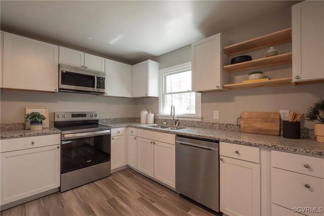 kitchen with light stone countertops, wood finished floors, a sink, white cabinets, and stainless steel appliances