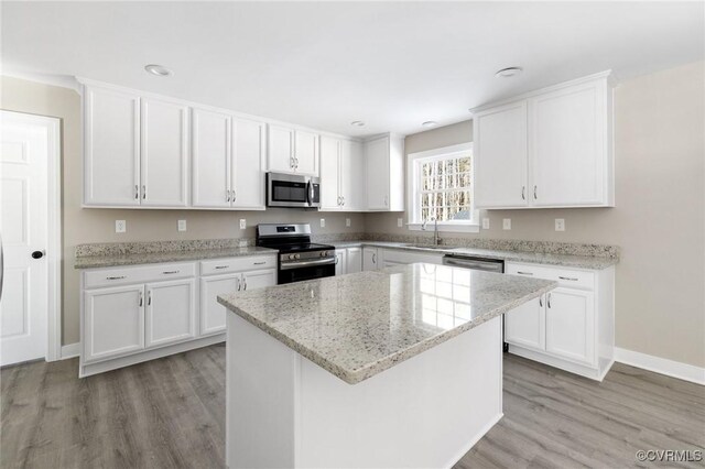 kitchen featuring white cabinets, a sink, light wood-style flooring, stainless steel appliances, and a kitchen island