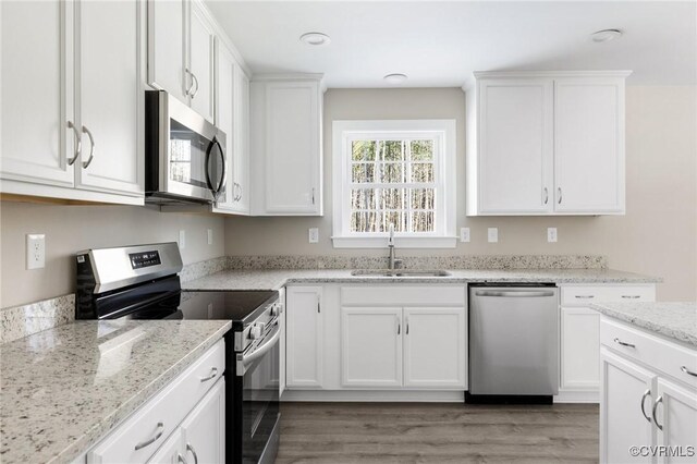 kitchen featuring light wood-type flooring, a sink, light stone counters, white cabinets, and stainless steel appliances