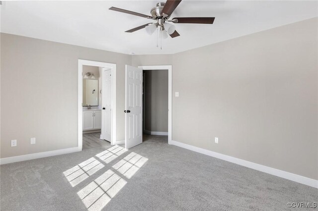 unfurnished bedroom featuring a ceiling fan, baseboards, light colored carpet, and ensuite bath