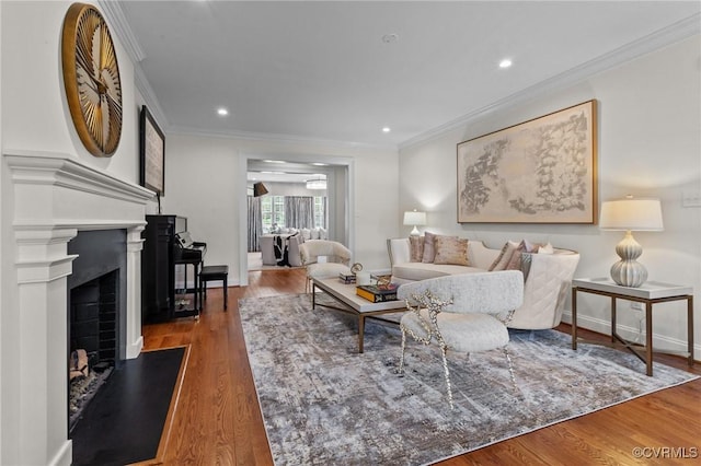 living room featuring ornamental molding, a fireplace with raised hearth, recessed lighting, and wood finished floors