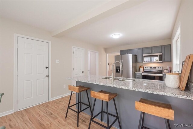 kitchen featuring a peninsula, light stone counters, a sink, light wood finished floors, and appliances with stainless steel finishes
