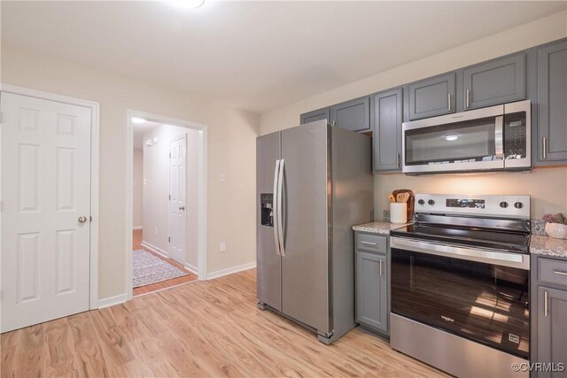 kitchen featuring light stone countertops, gray cabinets, light wood-style flooring, stainless steel appliances, and baseboards