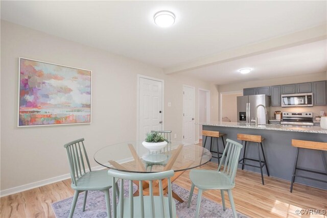 dining area featuring beamed ceiling, baseboards, and light wood-type flooring