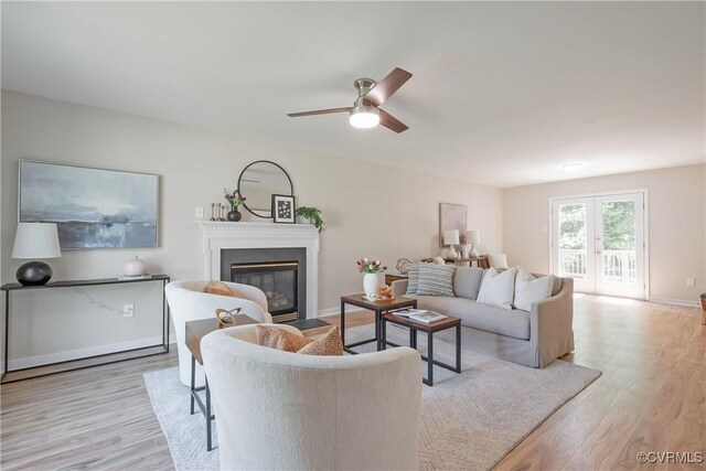 living room with a ceiling fan, baseboards, a fireplace with flush hearth, and wood finished floors