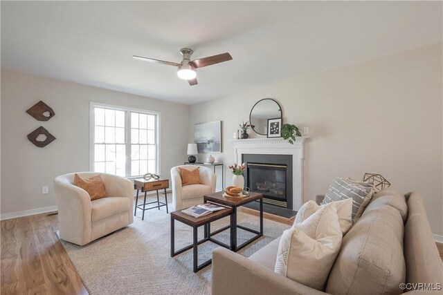 living area featuring a glass covered fireplace, baseboards, ceiling fan, and light wood finished floors