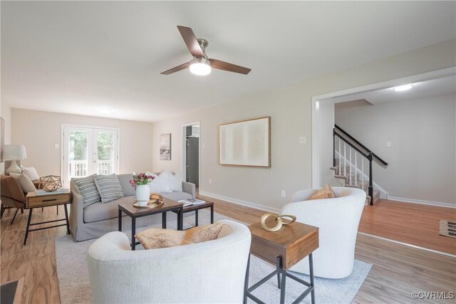 living room featuring stairs, a ceiling fan, baseboards, and light wood finished floors