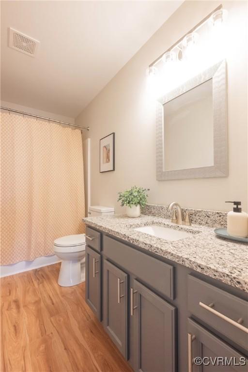 bathroom featuring visible vents, vanity, wood finished floors, toilet, and a shower with shower curtain