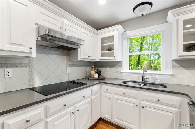 kitchen featuring dark countertops, a sink, black electric stovetop, under cabinet range hood, and white cabinetry