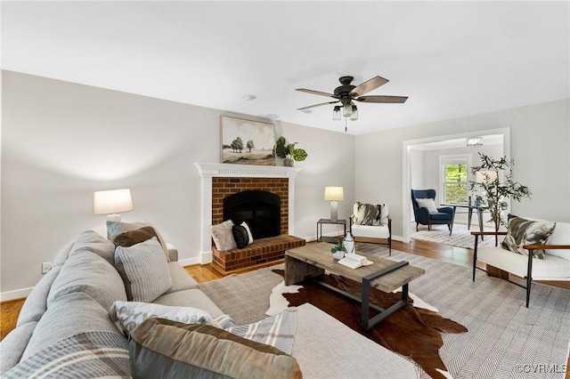 living area with baseboards, ceiling fan, a brick fireplace, and light wood-type flooring