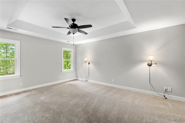 empty room with visible vents, carpet, baseboards, and a tray ceiling