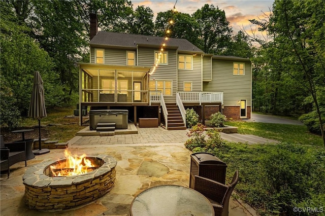 back of property featuring an outdoor fire pit, a chimney, a sunroom, a patio area, and a hot tub