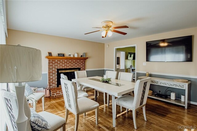 dining area with ceiling fan, a brick fireplace, and wood finished floors