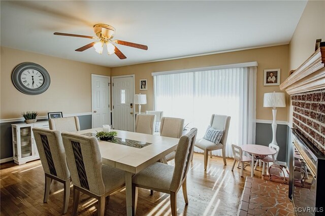 dining room with a ceiling fan, baseboards, wood finished floors, and a fireplace