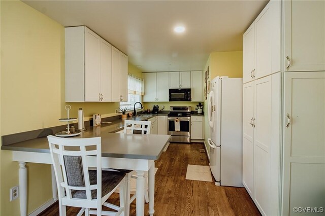 kitchen with freestanding refrigerator, stainless steel range with electric stovetop, a peninsula, black microwave, and a sink