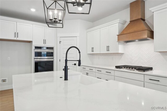 kitchen with decorative backsplash, gas stovetop, premium range hood, a notable chandelier, and white cabinetry