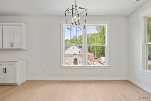 unfurnished dining area with baseboards, a notable chandelier, visible vents, and light wood-style floors