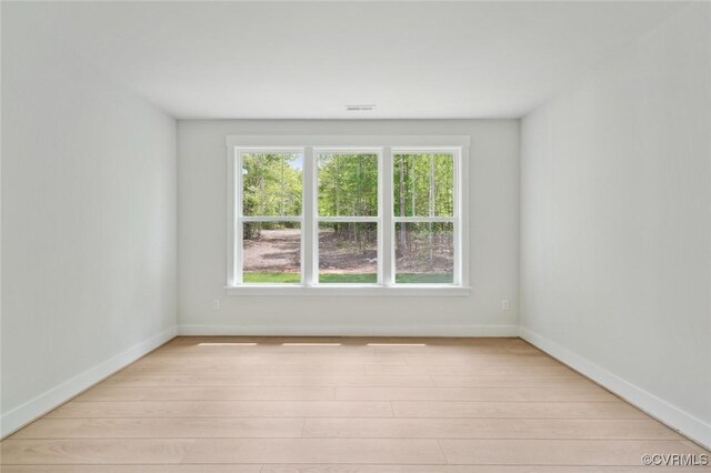 empty room featuring light wood-style floors, baseboards, and visible vents