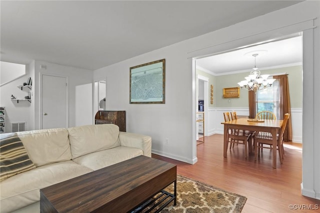 living area featuring crown molding, a notable chandelier, light wood-type flooring, and visible vents