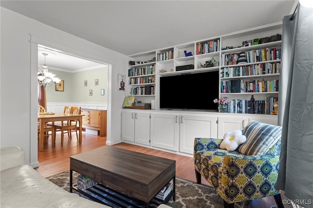 living room with a wainscoted wall, ornamental molding, light wood finished floors, and a notable chandelier