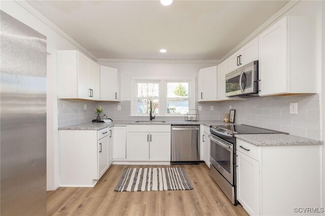 kitchen with a sink, appliances with stainless steel finishes, decorative backsplash, and light wood-style floors