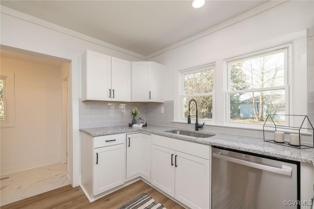 kitchen featuring backsplash, stainless steel dishwasher, light stone countertops, a sink, and white cabinetry