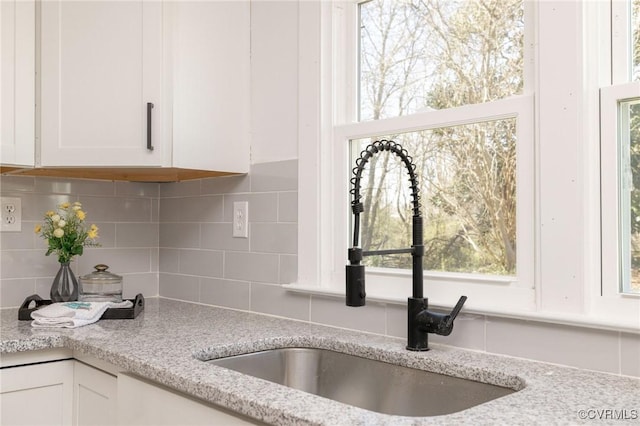 interior details with white cabinets, light stone counters, decorative backsplash, and a sink