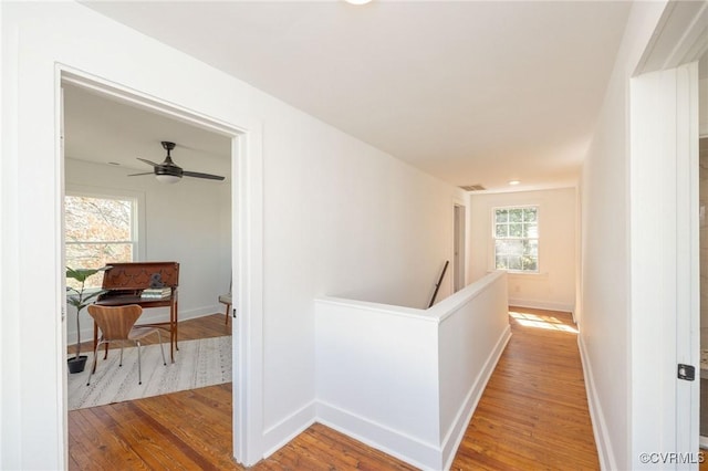 corridor featuring baseboards, wood finished floors, and an upstairs landing