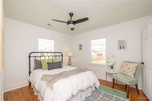 bedroom featuring baseboards, visible vents, multiple windows, and wood finished floors