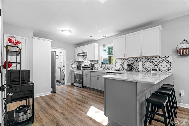 kitchen with decorative backsplash, a kitchen bar, a peninsula, under cabinet range hood, and stainless steel appliances