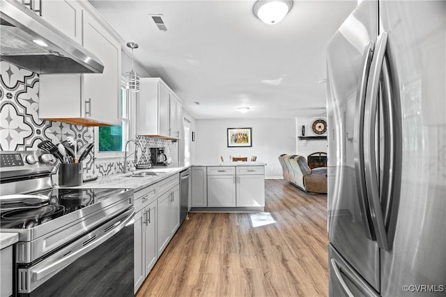 kitchen with a peninsula, open floor plan, under cabinet range hood, light wood finished floors, and stainless steel appliances