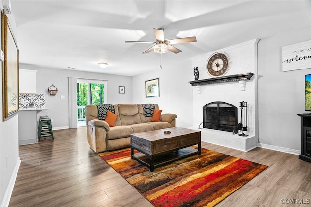 living area featuring baseboards, ceiling fan, wood finished floors, and a fireplace