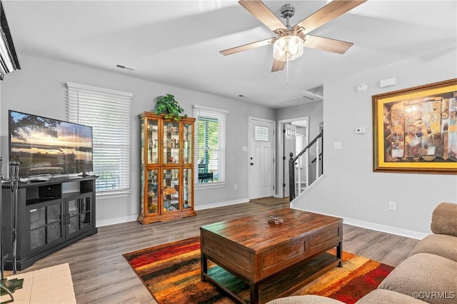 living room with ceiling fan, stairs, baseboards, wood finished floors, and visible vents