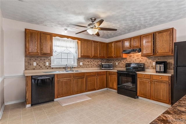 kitchen featuring brown cabinetry, a sink, baseboards, black appliances, and under cabinet range hood