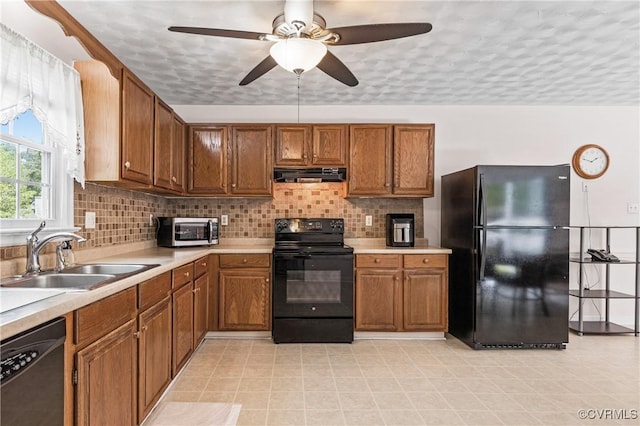 kitchen featuring a sink, light countertops, brown cabinetry, range hood, and black appliances