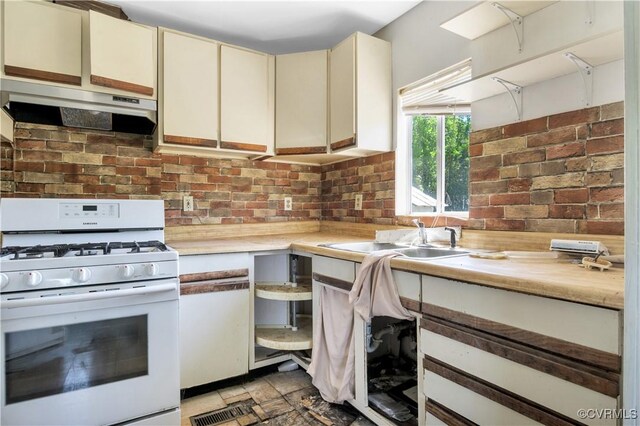 kitchen featuring gas range gas stove, light countertops, a sink, under cabinet range hood, and cream cabinetry