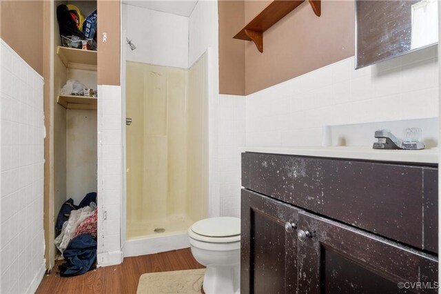 bathroom with vanity, toilet, tile walls, a shower stall, and wood finished floors