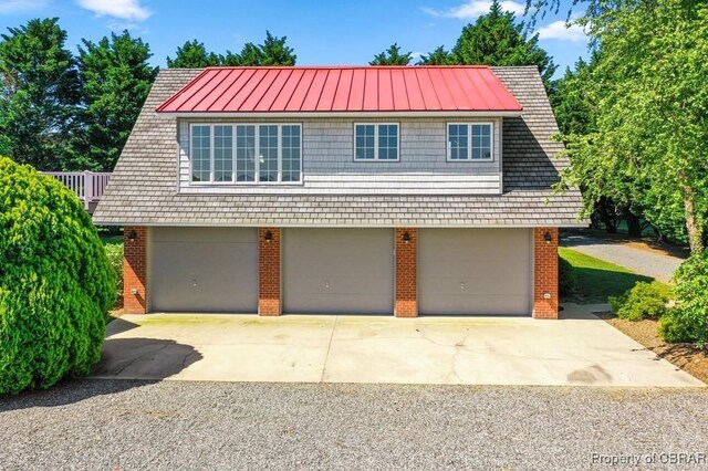 view of front facade with a standing seam roof, a garage, metal roof, and brick siding