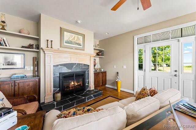 living area featuring baseboards, a premium fireplace, ceiling fan, and wood finished floors