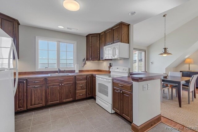 kitchen with dark countertops, hanging light fixtures, a sink, white appliances, and a peninsula