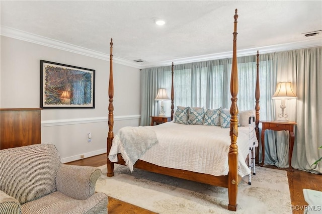 bedroom with visible vents, wood finished floors, baseboards, and ornamental molding