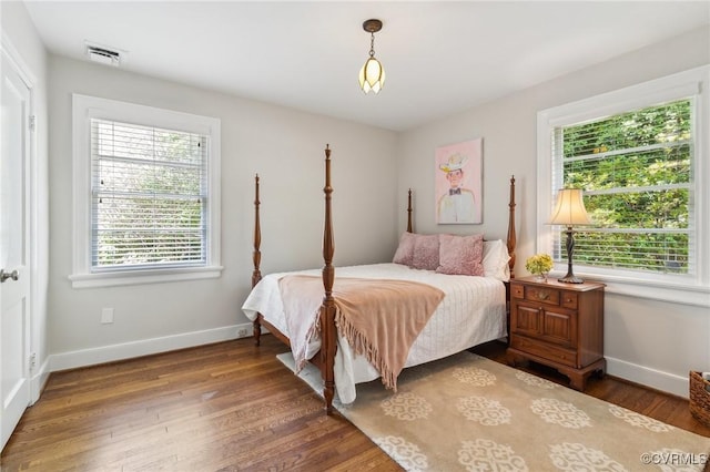 bedroom featuring baseboards, multiple windows, visible vents, and wood finished floors