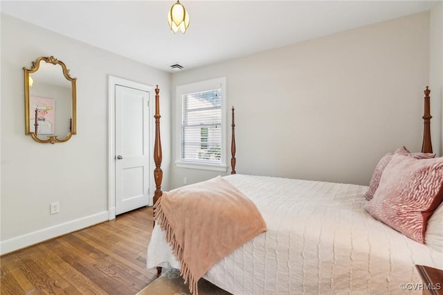 bedroom with baseboards, visible vents, and wood finished floors