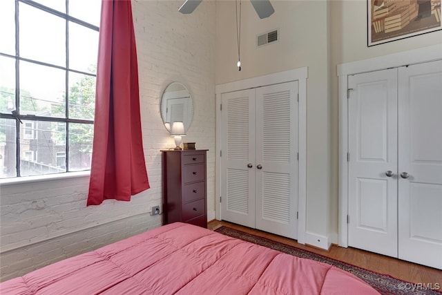 bedroom featuring brick wall, a high ceiling, wood finished floors, and visible vents