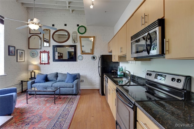 kitchen featuring appliances with stainless steel finishes, a sink, light wood-style floors, brick wall, and open floor plan