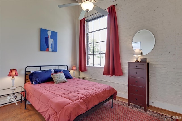 bedroom with baseboards, wood finished floors, brick wall, and multiple windows
