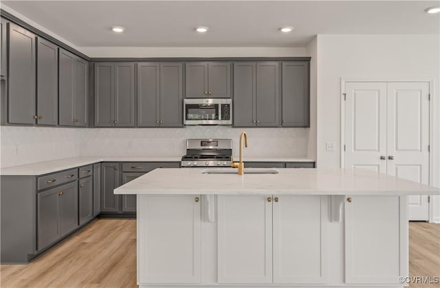 kitchen featuring gray cabinets, appliances with stainless steel finishes, light wood-type flooring, a sink, and light stone counters