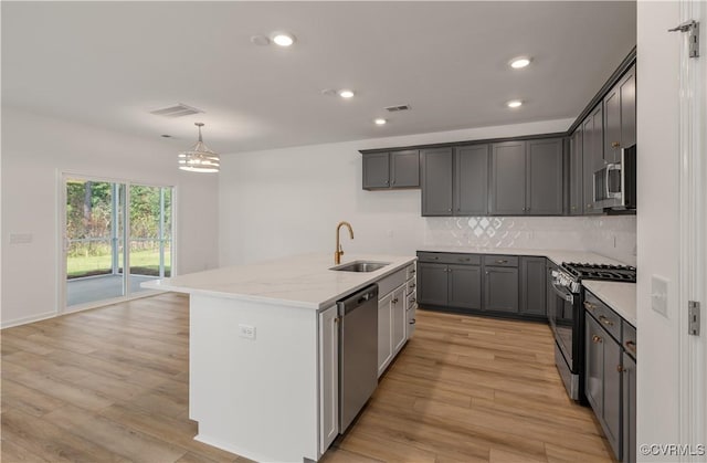 kitchen with stainless steel appliances, tasteful backsplash, a sink, and light wood-style floors