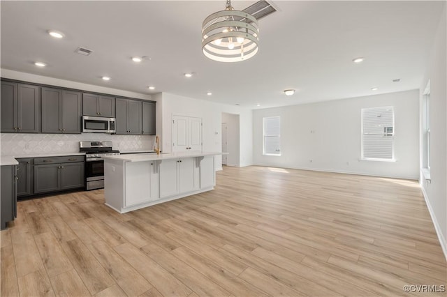 kitchen featuring light wood-type flooring, decorative backsplash, an inviting chandelier, and stainless steel appliances